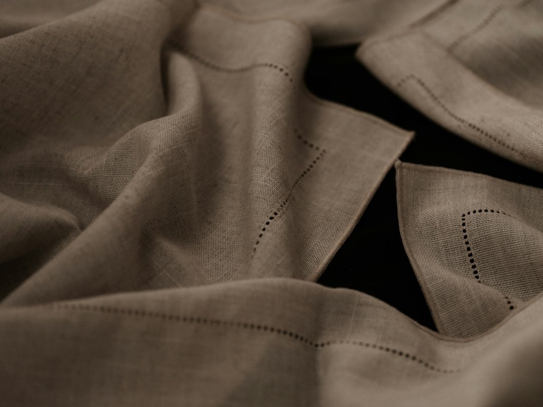 Draped taupe linen fabric with hemstitched edging photographed in low, moody light.