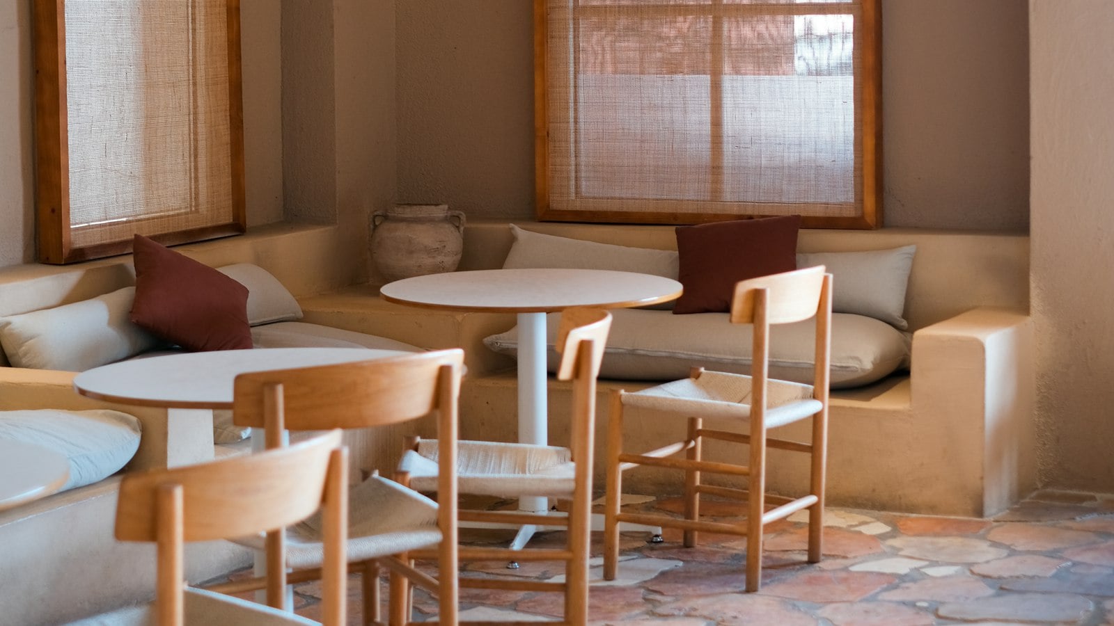 A cosy café corner with built-in bench seating, cushions, round tables and wooden chairs (photo: Finn / Unsplash)