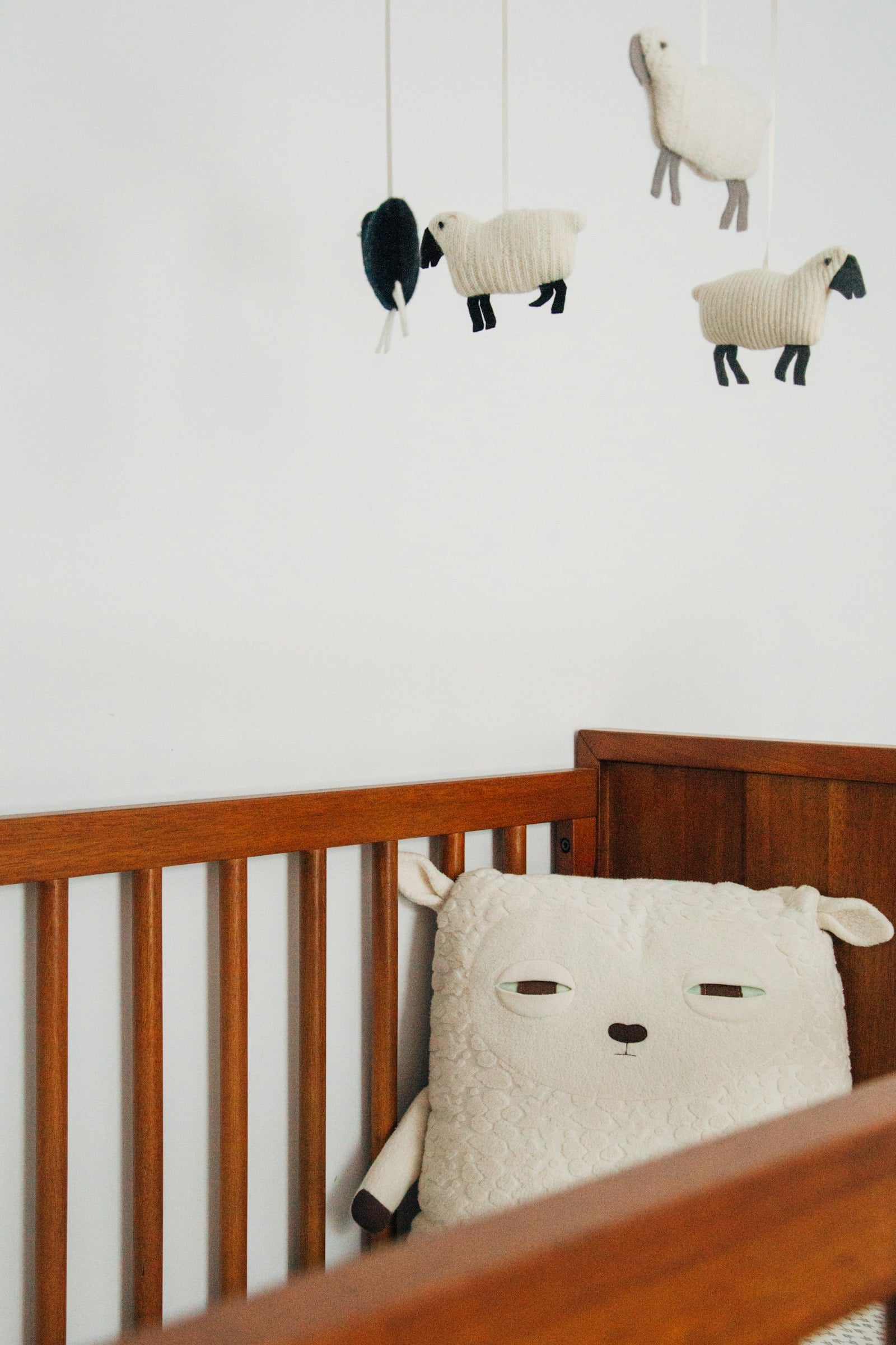 Wooden crib with a soft toy and a felt sheep mobile (photo: charlesdeluvio / Unsplash)
