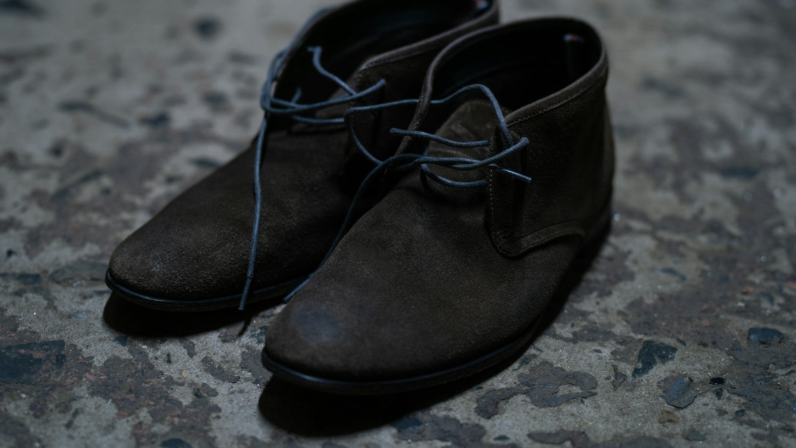 Dark suede lace-up ankle boots resting on weathered stone (photo: maks_d / Unsplash)