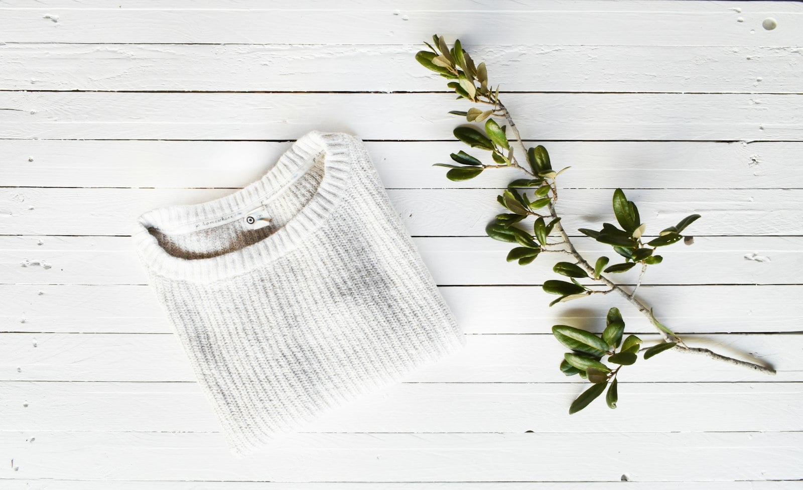 White knitted baby top on a white wooden table with a sprig of leaves (photo: Shelter / Unsplash)