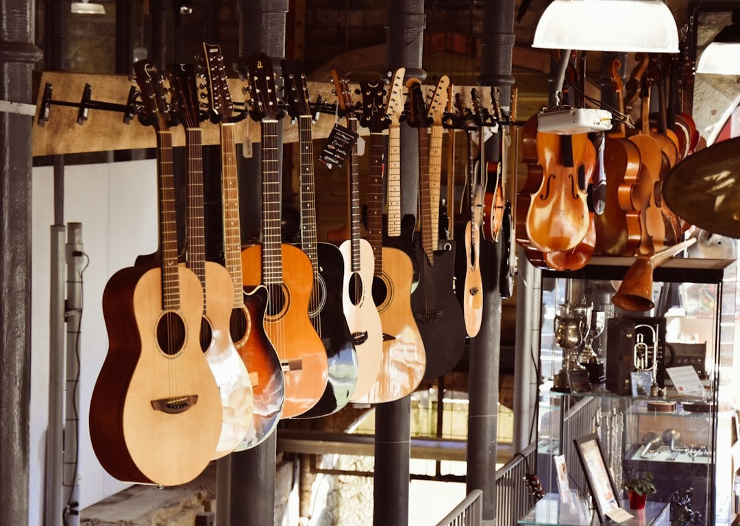 Acoustic guitars hanging in a row inside a music shop with violins and glass display cases in the background