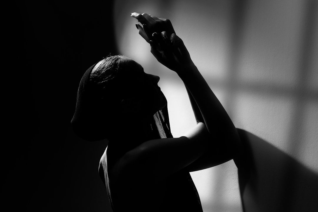 Dramatic black-and-white silhouette of a person tilting their head back while spraying a mist overhead