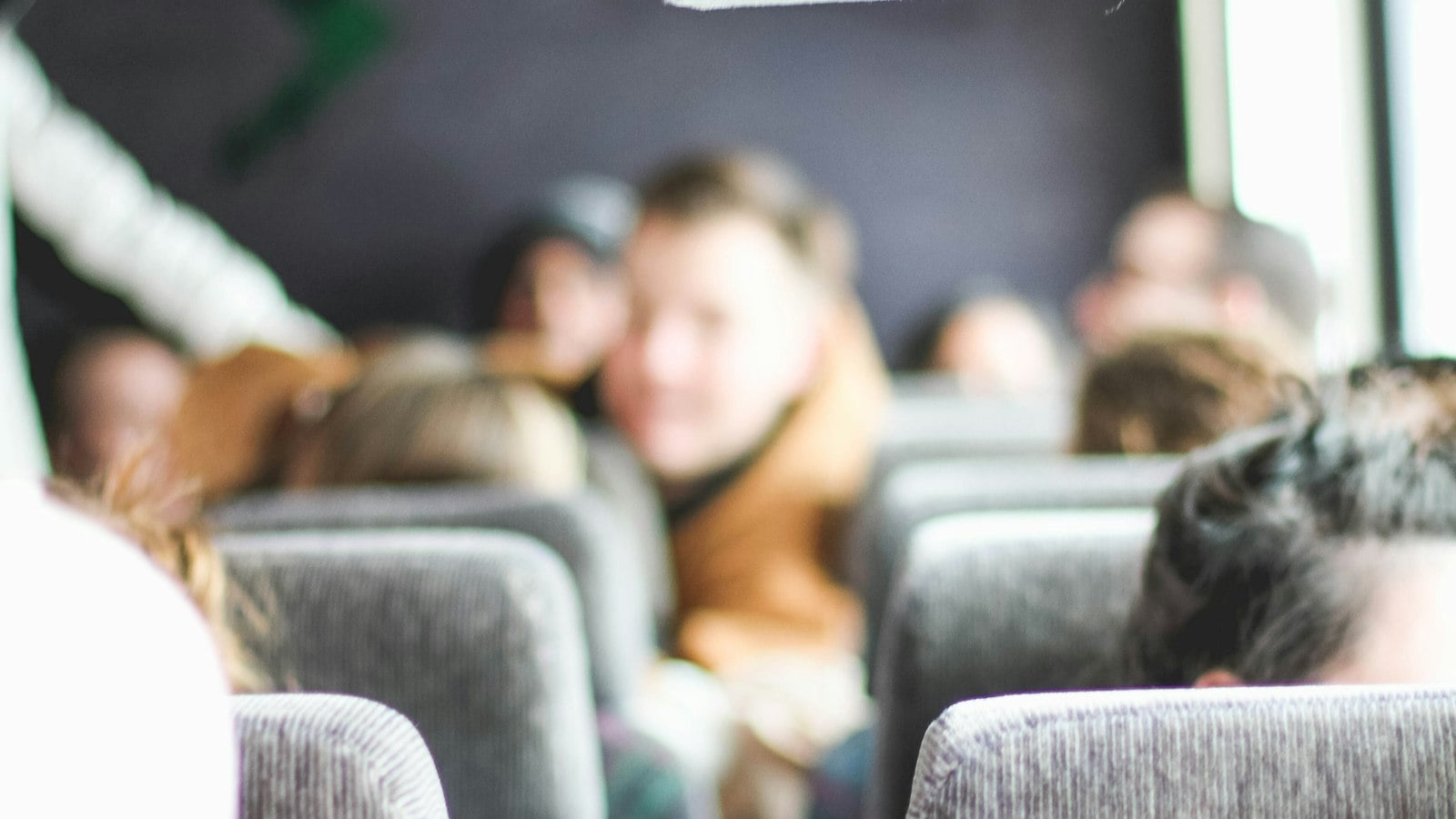 Passengers sitting in rows of seats inside a moving coach, seen from behind