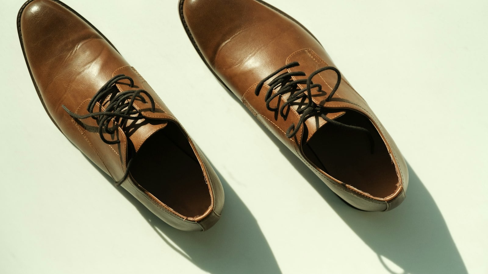 A pair of tan leather derby shoes photographed from directly above on a pale green surface (photo: Ty Feague / Unsplash)
