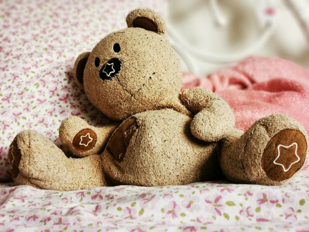 A soft brown teddy bear lies on floral bedding beside a pink blanket
