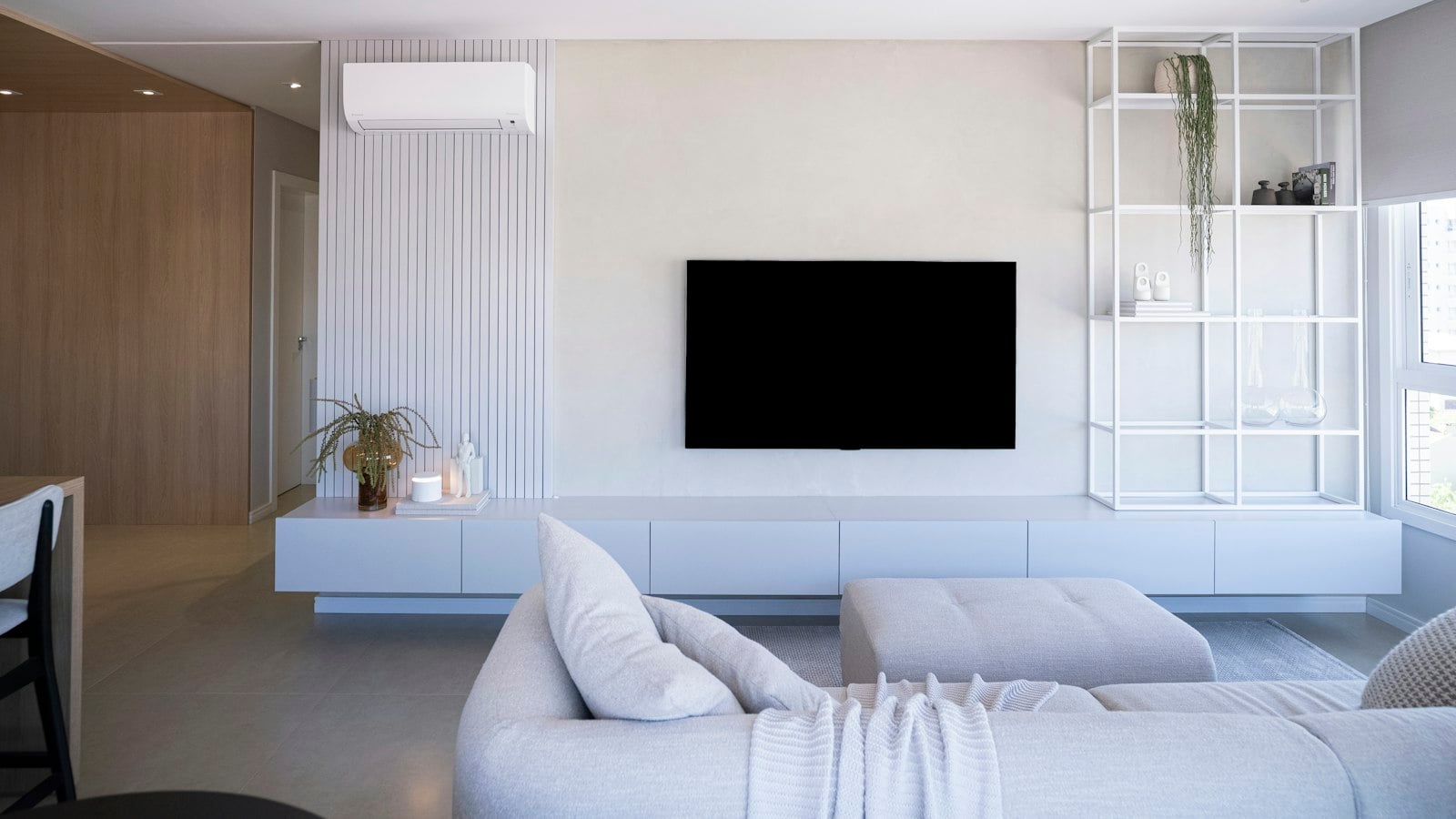A large wall-mounted TV above a low white media unit in a minimal, light-filled living room (photo: Caroline Badran / Unsplash)