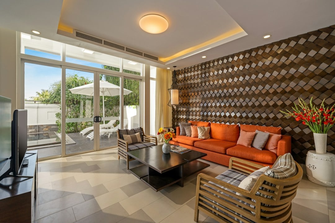 A modern resort condo living room with an orange sofa, TV and sliding doors to a sunny patio
