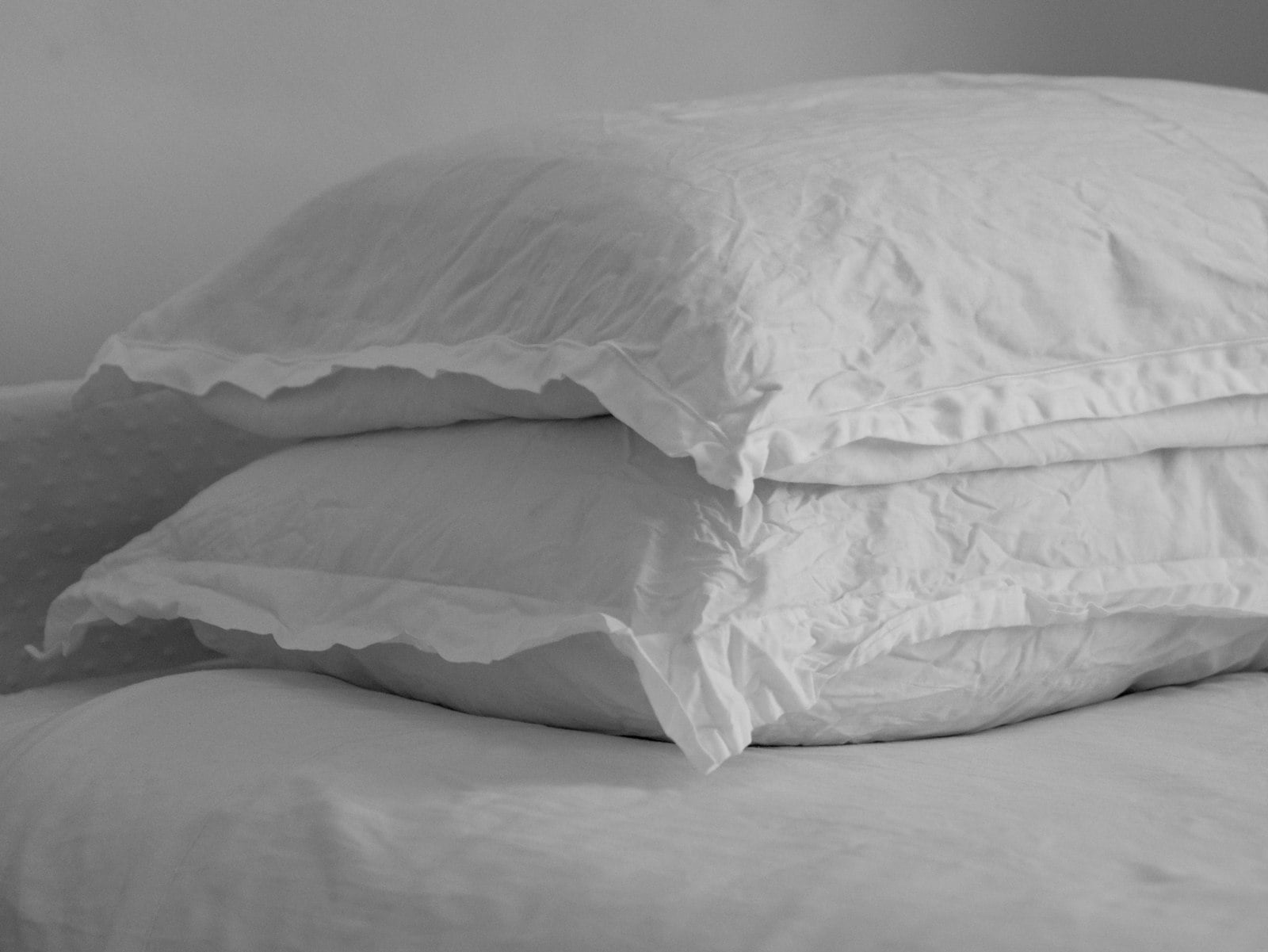 Two white pillows stacked on a made bed (photo: the blowup / Unsplash)